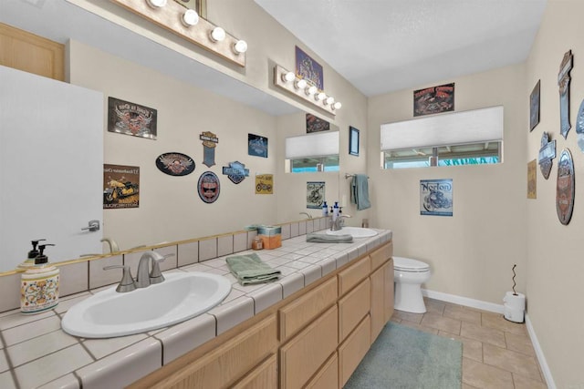 full bathroom with tile patterned flooring, toilet, a sink, baseboards, and double vanity