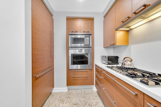 kitchen featuring brown cabinetry, modern cabinets, light countertops, stainless steel gas cooktop, and light speckled floor