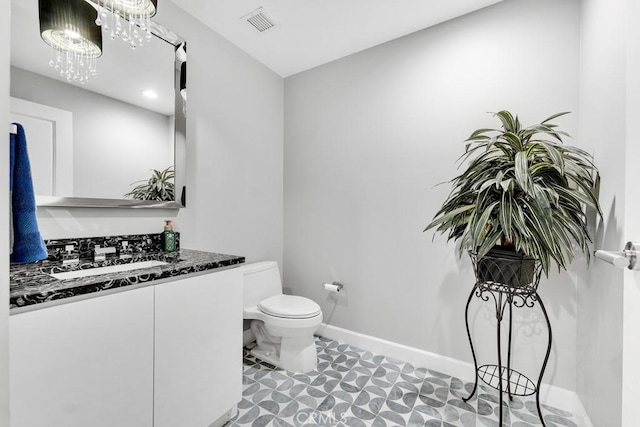 bathroom featuring toilet, vanity, visible vents, and baseboards