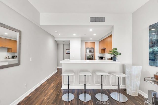 kitchen with stainless steel appliances, a breakfast bar, dark wood finished floors, and visible vents