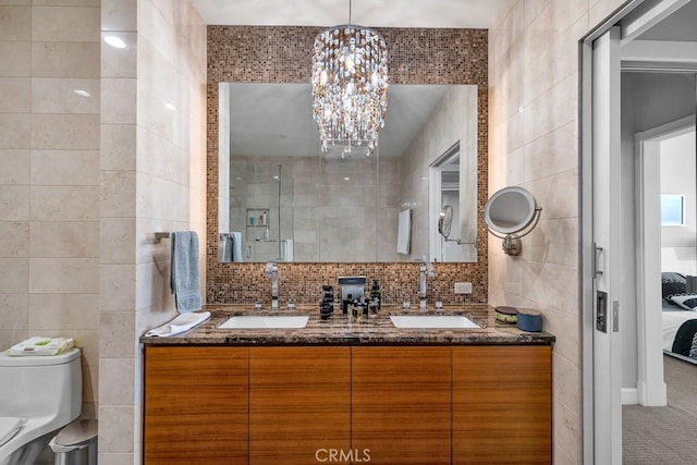 bathroom featuring a sink, a chandelier, toilet, and tile walls