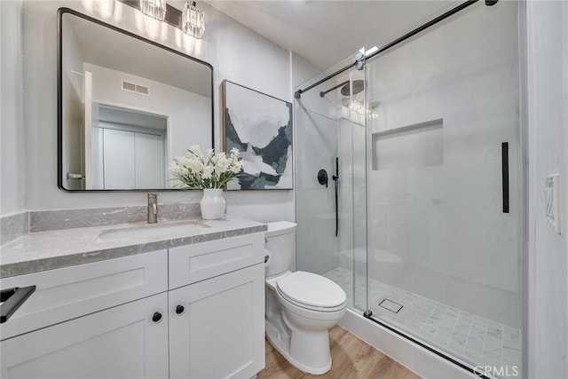 full bathroom featuring toilet, wood finished floors, visible vents, vanity, and a shower stall