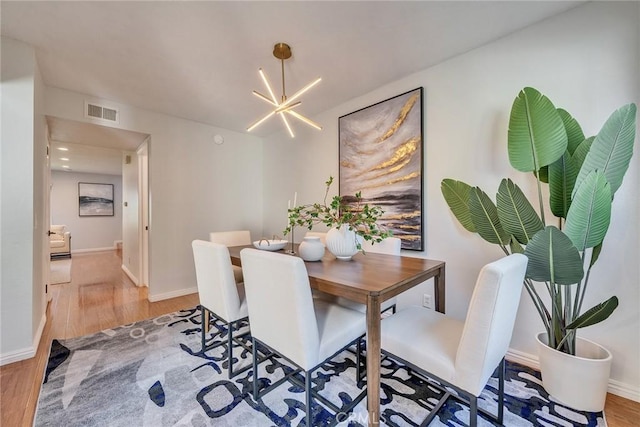 dining room featuring visible vents, a notable chandelier, baseboards, and wood finished floors