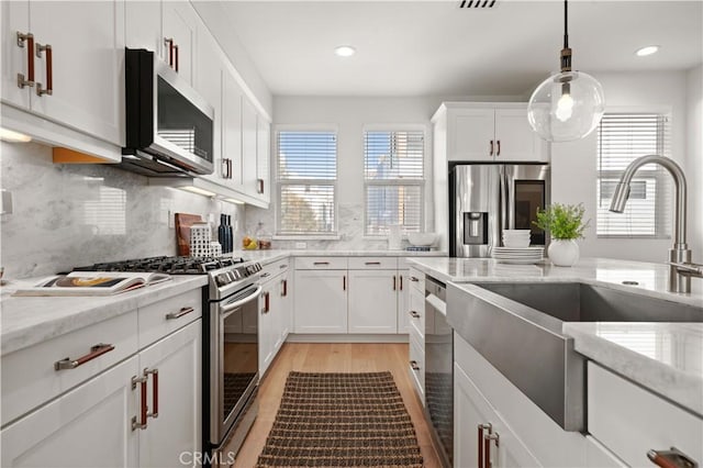 kitchen featuring a sink, stainless steel appliances, light wood-style floors, white cabinets, and decorative backsplash