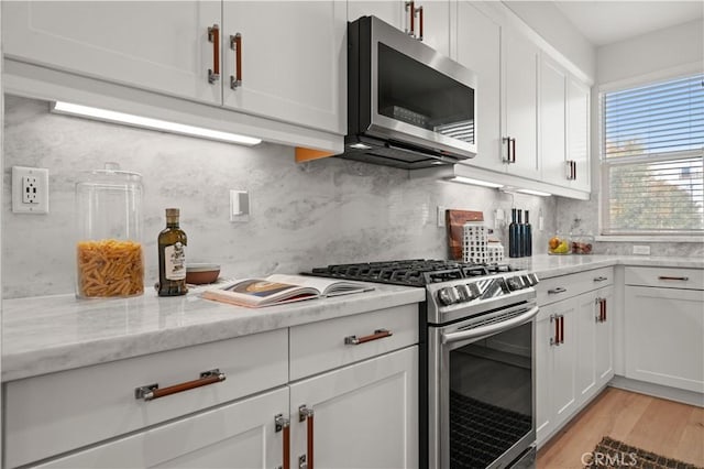 kitchen with light stone counters, decorative backsplash, appliances with stainless steel finishes, light wood-style floors, and white cabinetry