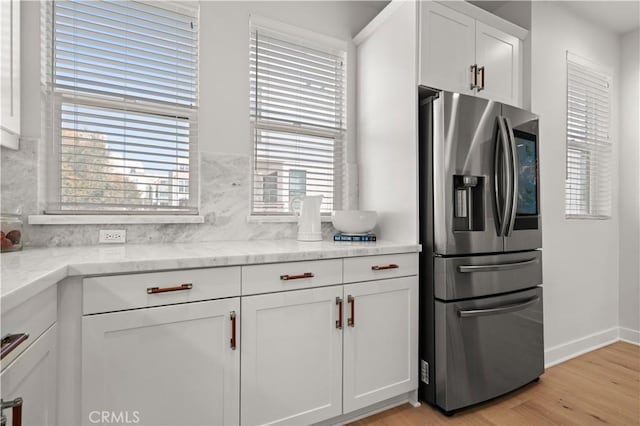 kitchen featuring light stone countertops, stainless steel fridge with ice dispenser, decorative backsplash, light wood-style floors, and white cabinetry