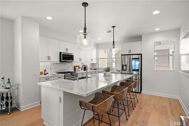 kitchen with light wood-type flooring, visible vents, a sink, backsplash, and stainless steel appliances