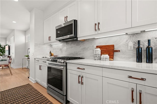 kitchen featuring light stone countertops, baseboards, light wood finished floors, stainless steel appliances, and white cabinetry