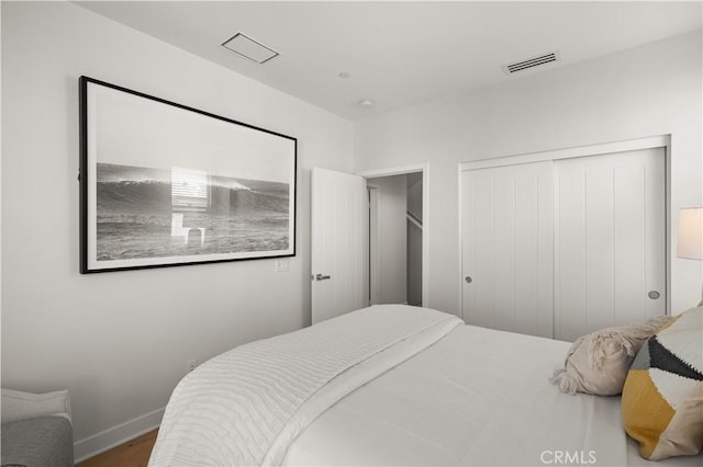 bedroom with wood finished floors, visible vents, a closet, and baseboards