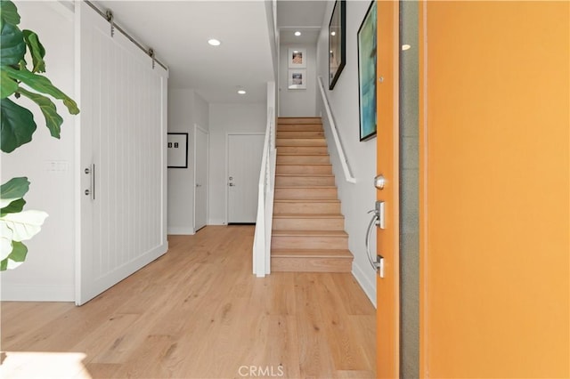 entryway with baseboards, recessed lighting, stairs, light wood-style floors, and a barn door