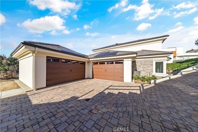 view of front of house with a garage, solar panels, stone siding, decorative driveway, and stucco siding