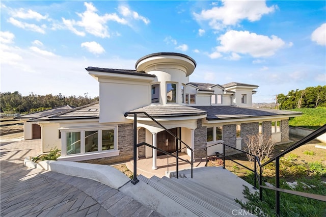 rear view of house featuring stone siding, a patio, and stucco siding