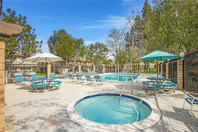 community pool with a hot tub, fence, and a patio