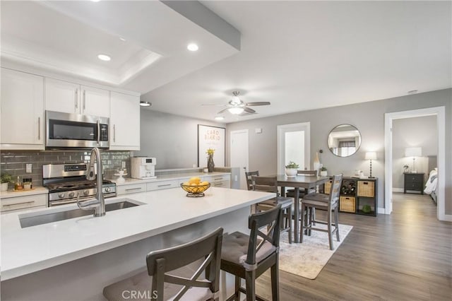 kitchen featuring dark wood-style flooring, stainless steel appliances, light countertops, decorative backsplash, and a kitchen bar