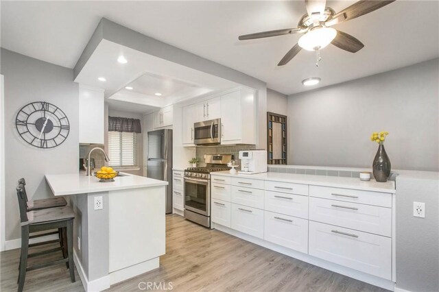 kitchen with white cabinets, a peninsula, stainless steel appliances, light wood-type flooring, and a sink