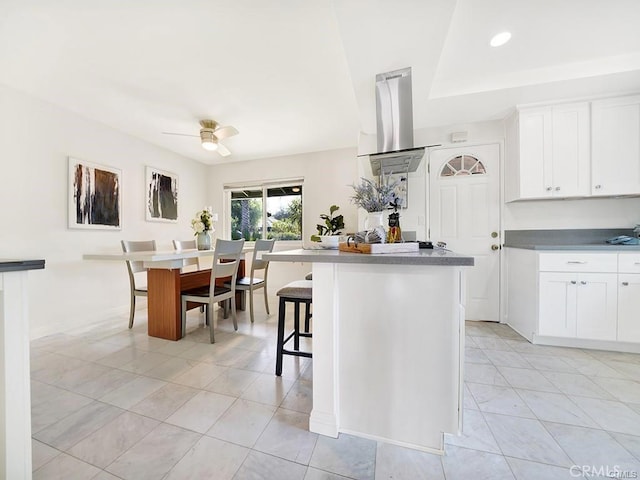 kitchen with a ceiling fan, white cabinetry, island exhaust hood, and a kitchen bar