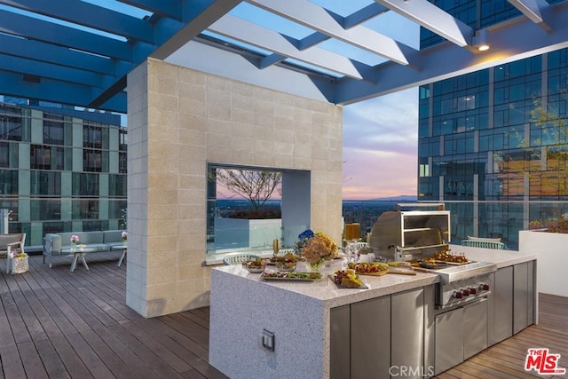 deck at dusk featuring an outdoor kitchen and a pergola