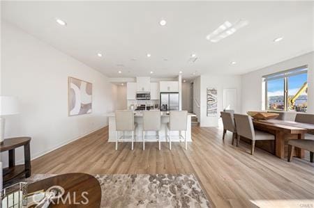 kitchen featuring a breakfast bar area, light wood-style flooring, white cabinetry, stainless steel fridge with ice dispenser, and an island with sink