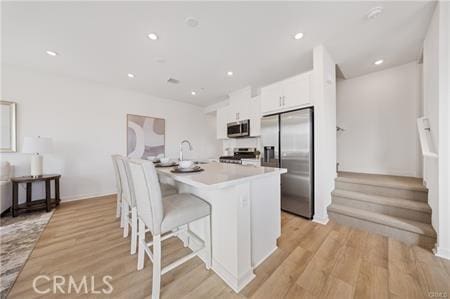 kitchen with light wood-type flooring, white cabinetry, appliances with stainless steel finishes, and light countertops