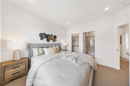 bedroom with baseboards, visible vents, light colored carpet, a walk in closet, and recessed lighting