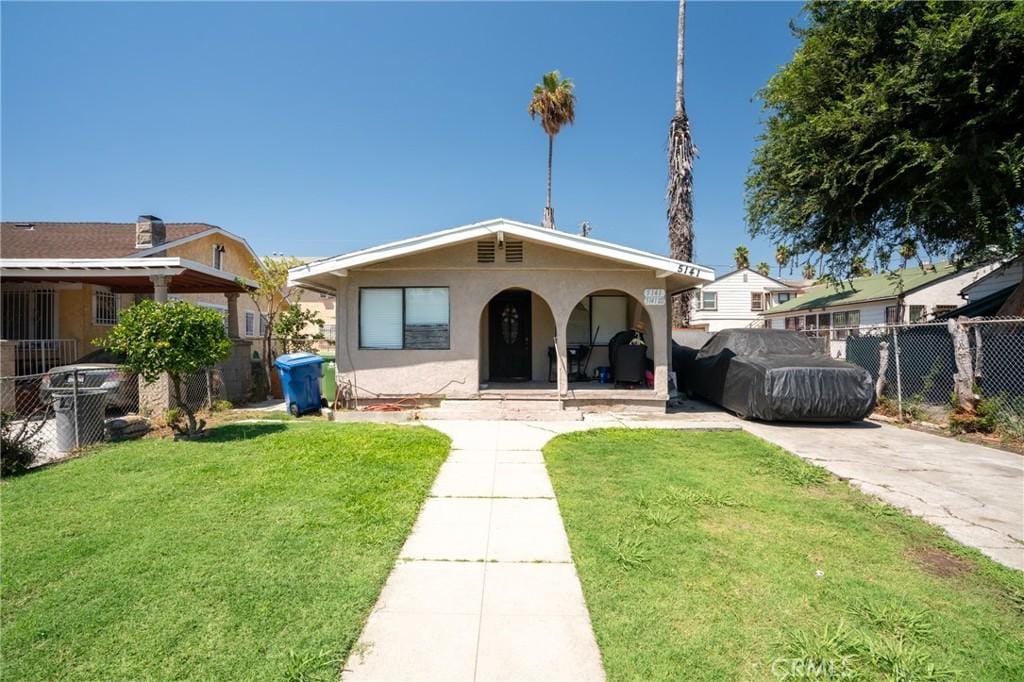 bungalow-style house with a porch, a front yard, fence, and stucco siding