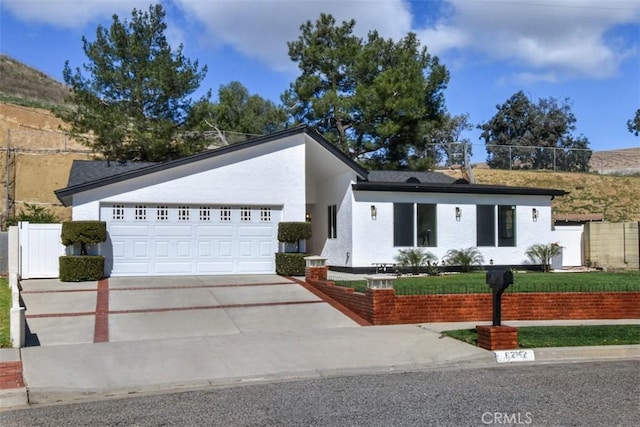 view of front facade featuring driveway, an attached garage, fence, and stucco siding