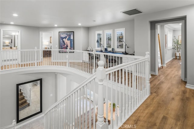 hallway featuring a healthy amount of sunlight, visible vents, wood finished floors, and an upstairs landing