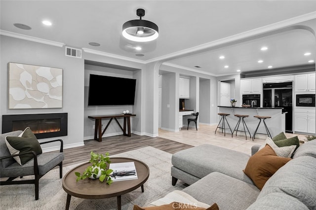 living area with recessed lighting, visible vents, light wood-style floors, a glass covered fireplace, and crown molding