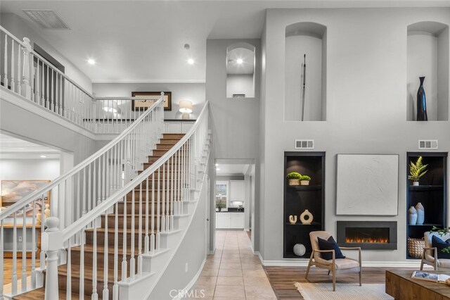 stairs featuring a lit fireplace, a towering ceiling, visible vents, and baseboards