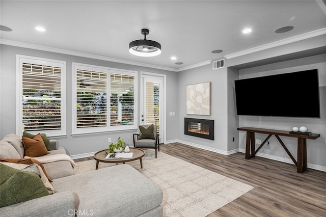 living area featuring ornamental molding, a glass covered fireplace, visible vents, and plenty of natural light