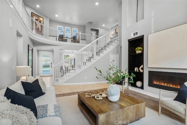 living room with a towering ceiling, stairway, a glass covered fireplace, and visible vents