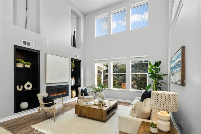 living room with a warm lit fireplace, visible vents, and wood finished floors