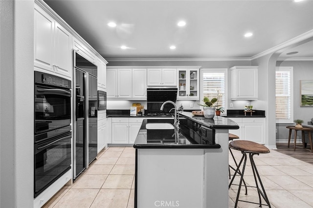 kitchen featuring light tile patterned floors, dark countertops, ornamental molding, a sink, and a kitchen bar