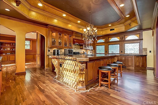 bar with arched walkways, a tray ceiling, stainless steel microwave, and dark wood-style floors