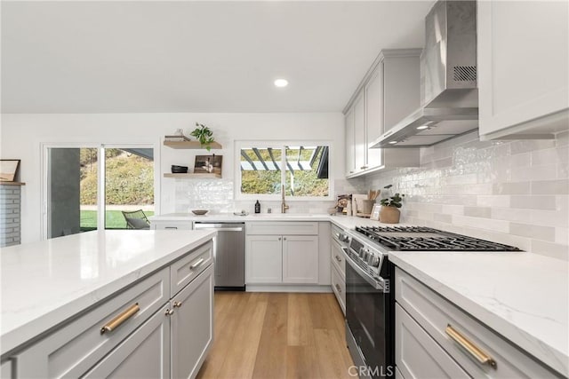 kitchen with open shelves, light wood-style floors, appliances with stainless steel finishes, wall chimney range hood, and decorative backsplash