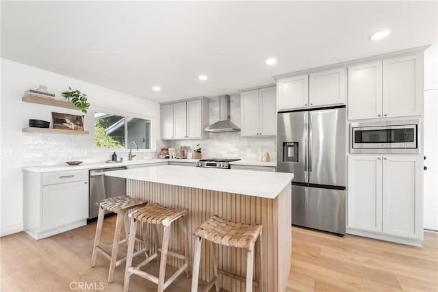 kitchen with a breakfast bar area, open shelves, stainless steel appliances, wall chimney range hood, and a center island