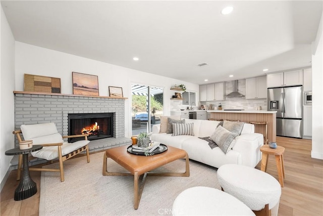 living room featuring recessed lighting, light wood-style flooring, a brick fireplace, and visible vents