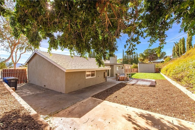 view of side of property featuring stucco siding, a patio, a shed, fence, and an outdoor structure