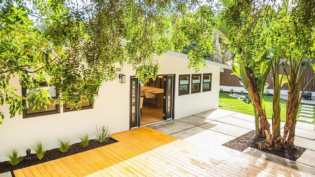 entrance to property featuring a lawn, a deck, and stucco siding