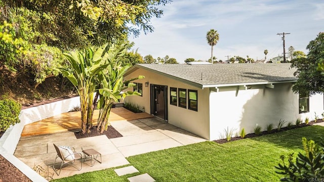 exterior space featuring a patio area, roof with shingles, a front yard, and stucco siding