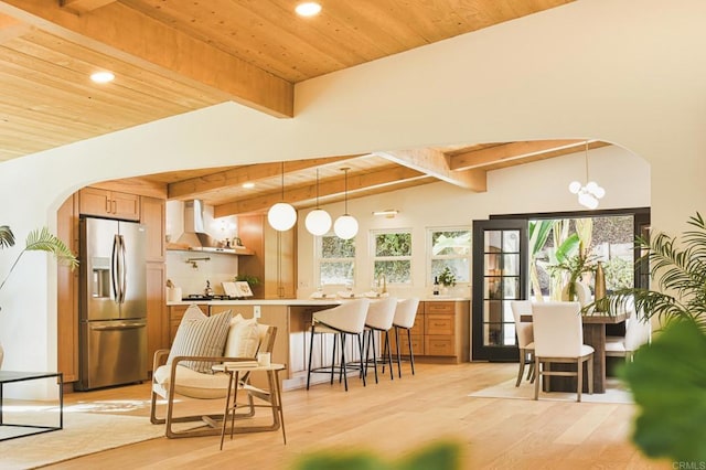 kitchen featuring arched walkways, wall chimney range hood, stainless steel refrigerator with ice dispenser, and wooden ceiling