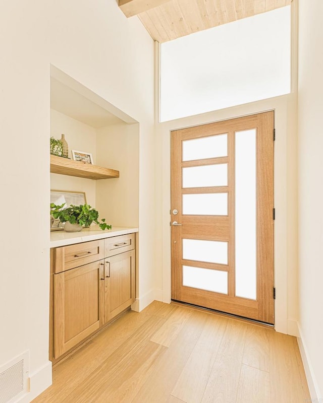 doorway featuring visible vents, a healthy amount of sunlight, baseboards, light wood-type flooring, and beam ceiling