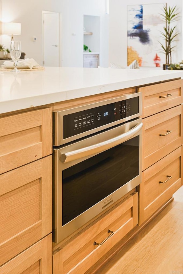 kitchen with light countertops, light brown cabinetry, stainless steel oven, and light wood-style floors