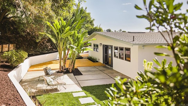 rear view of property featuring a shingled roof, a patio, a deck, and stucco siding