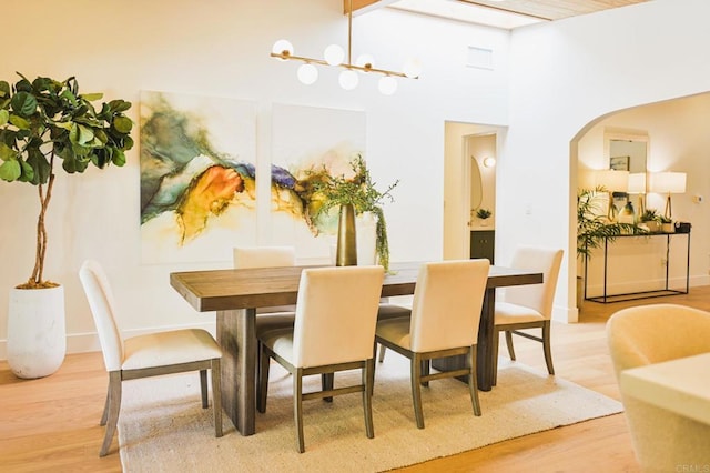 dining space featuring light wood finished floors, baseboards, arched walkways, and a notable chandelier