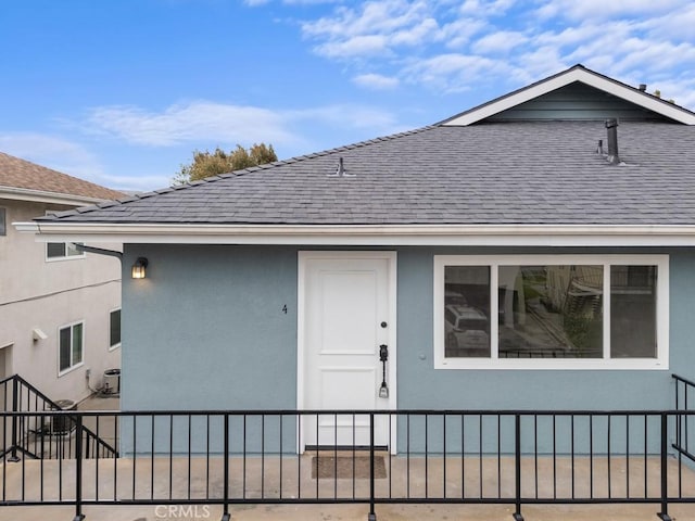 exterior space featuring stucco siding, fence, and roof with shingles