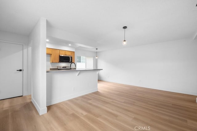 kitchen featuring a peninsula, light wood-style floors, stainless steel microwave, and a kitchen breakfast bar