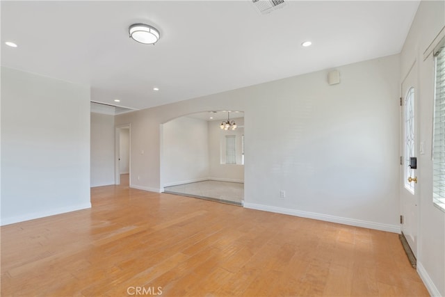 empty room with baseboards, light wood-type flooring, arched walkways, and recessed lighting