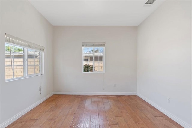 empty room with visible vents, light wood-style flooring, and baseboards