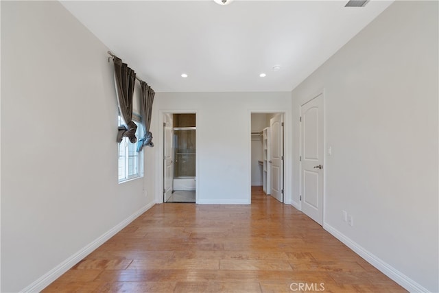 unfurnished bedroom featuring a walk in closet, baseboards, light wood finished floors, and ensuite bathroom